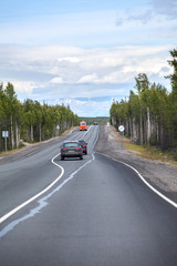 Highway stretches away to mountains on horizon. Passenger cars driving on the Kola asphalt road. It is way to the Murmansk city on north of Russia