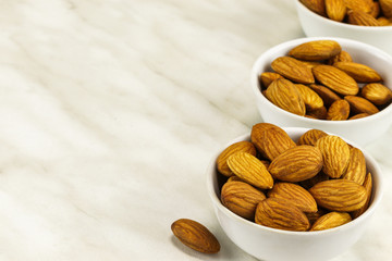 Almonds in three white bowls on a white marble surface on the right