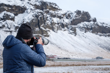 Fototapeta na wymiar A photographer uses his tele photo to capture an epic moment in the snow. The man is wearing blue coat and black hat. The image is taken in Iceland.
