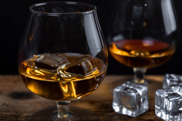 Two whiskey / cognac glasses with ice on a wooden background. Dark backdrop.