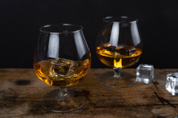 Two whiskey / cognac glasses with ice on a wooden background. Dark backdrop.