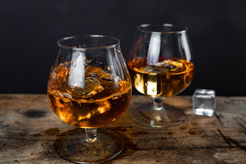 Two whiskey / cognac glasses with ice on a wooden background. Dark backdrop.