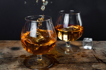 Two whiskey / cognac glasses with ice on a wooden background. Dark backdrop.