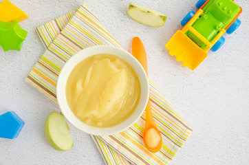 Baby food. Homemade apple puree or sauce from organic apples in a bowl with a spoon on a light background with fresh apples. Horizontal orientation. Top view. Copy space