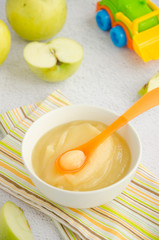Baby food. Homemade apple puree or sauce from organic apples in a bowl with a spoon on a light background with fresh apples. Vertical orientation. Close up