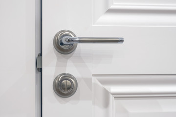 Metal handle with a rotary lock on a white half-open door, close-up. The element door in the style of French Provence