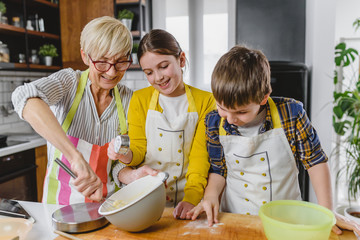 Grandmother and her grandchildren making cakes together in the home kitchen. Children helping...