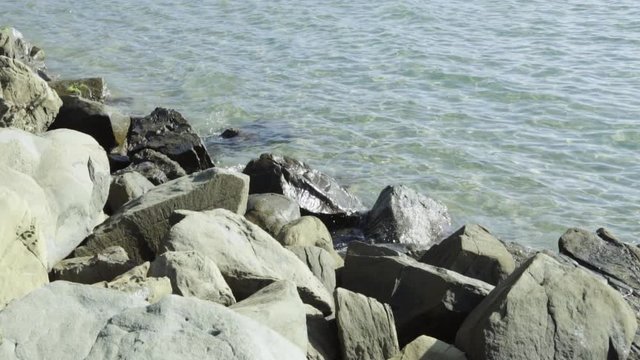 Wave move towards shore and splash on rough stones of breakwater, slow motion shot