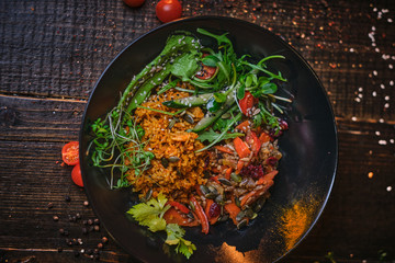 Hot, vegetarian plate of meal which includes cooked vegetarian pilaf served with healthy mix of ruccola leafs, bulgarian pepper, thin sliced vegetables, cherry tomatoes and spices, on a black