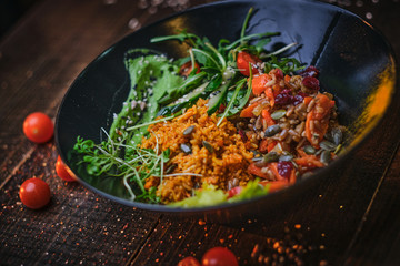 Tasty, vegetarian plate of meal which includes cooked vegetarian pilaf served with healthy mix of ruccola leafs, bulgarian pepper, thin sliced vegetables, cherry tomatoes and spices, on a black