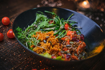 Traditional, vegetarian plate of meal which includes cooked vegetarian pilaf served with healthy mix of ruccola leafs, bulgarian pepper, thin sliced vegetables, cherry tomatoes and spices, on a black