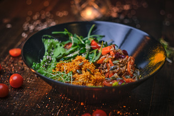 Healthy, vegetarian plate of meal which includes cooked vegetarian pilaf served with healthy mix of ruccola leafs, bulgarian pepper, thin sliced vegetables, cherry tomatoes and spices, on a black