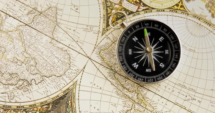 Disorientated spinning compass against map background closeup footage