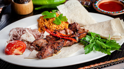 Turkish cuisine. Halal veal kebab with bulgur porridge, grilled vegetables on pita bread. Serving dishes in a restaurant on a white plate. background image, copy space text