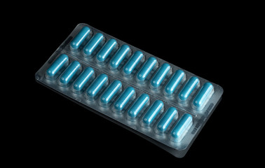 Blue medical capsules in blisters isolated on a black mirror background.