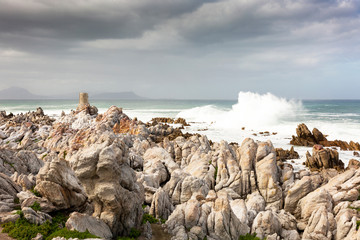 Waves smashing in rocky coast of the sea with small historic structure in Betty's Bay, South Africa