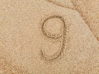 Fototapeta na wymiar The number 9 on wet beach sand. 