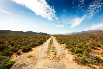 Fototapeta na wymiar Scenic gravel road in African nature along route 62 with gradient blue cloudy sky 