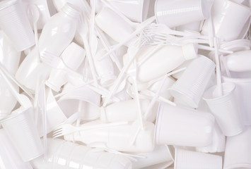 Disposable white single use plastic objects such as bottles, cups, forks and spoons that cause pollution of the environment, especially oceans. Top view.