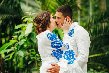 Lovely couple in white suits with blue embroidery posing against palm tree background