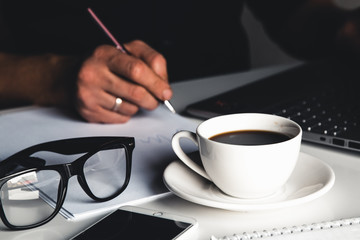 A man types on a laptop, business concept, glasses, a cup of coffee and a pen on a gray background.