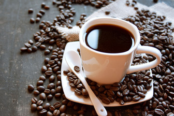 Czarna kawa w białej filiżance na tle rozsypanych ziaren kawy