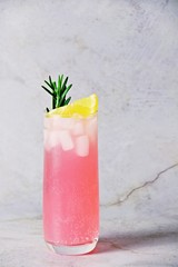 Refreshing glass of rose lemonade with ice cubes, lemon and rosemary