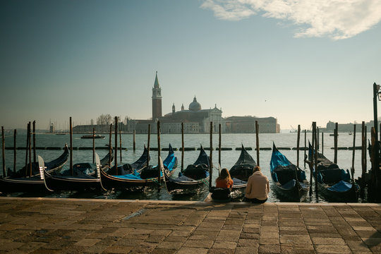 Mujeres sentadas a la orilla del mar en Venecia frene a las g&oacute;ndolas