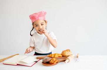 Asian little chef girl test the taste of bread on the table by pick some piece and eat with white background.