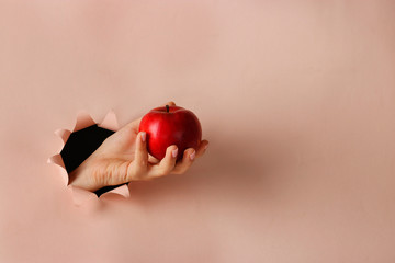 Ripe red apple in a female hand through round hole in pink paper, Copy space