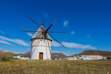 traditional windmill and behind the village of El Pozo de los Frailes, windmill traditional in Spain, Pozo de los Frailes, province of Almeria, windmill under blue sky