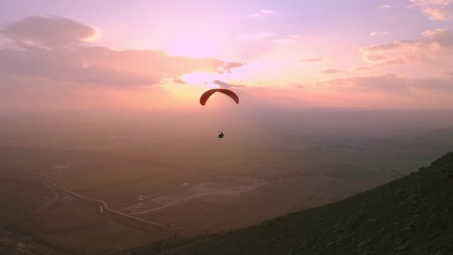 Lonely silhouette of pilot fly on parachute in sunset. Beautiful epic pink sunset over mountains. Professional paraglider enjoys fresh air and extreme adrenaline while in air