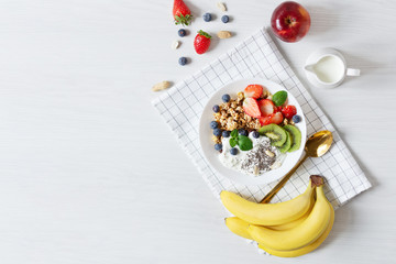 White ceramic bowl of homemade granola with yogurt, fresh berries and fruits on white wooden table background top view.