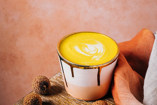 Golden milk latte in pink and gold cup with tumeric and ginger