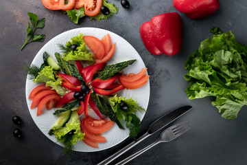 tomato, bell pepper, cucumber slices, lettuce and thyme on white plate, served on grey background in rustic style with copy space, sliced raw assorted vegetables in food restaurant, horizontal photo