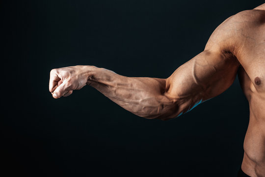 tense arm clenched into fist, veins, bodybuilder muscles on a dark background, isolate.