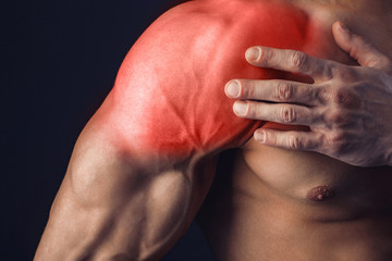 Bodybuilder suffering from shoulder pain on dark background. Isolate