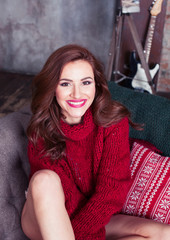 Fototapeta premium young pretty stylish woman in red winter sweater at couch in home interior happy smiling, lifestyle people concept