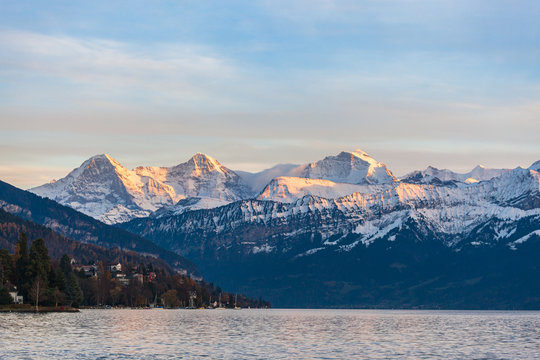 Stunning panorama view of famous Swiss Alps peaks on Bernese Oberland Eiger North Face, Monch, Jungfrau at sunset from Lake Thun (Thunersee) on a sunny autumn day with blue sky cloud,Bern, Switzerland
