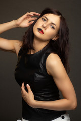 Naklejka premium a brunette in a black leather sleeveless blouse poses on a gray background