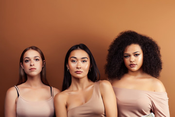 young pretty asian, caucasian, afro woman posing cheerful together on brown background, lifestyle diverse nationality people concept