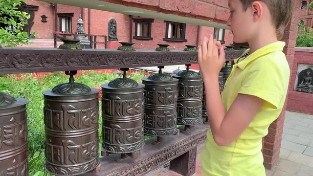 Caucasian boy touching, rotating nepalese traditional metal prayer wheels with mantra Om Mani Padme Hum, that means O, the jewel in the lotus, hanging in a row
