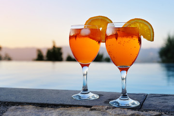 two glasses with Spritz Veneziano, an Italian cocktail drink from aperol, prosecco and soda on a wall at the water against a clear sunset sky, copy space