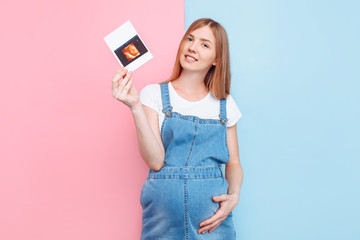 Naklejka premium Young attractive pregnant woman in denim overalls with ultrasound scan photo