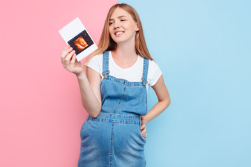 Naklejka premium Young attractive pregnant woman in denim overalls with ultrasound scan photo
