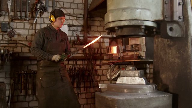 A man blacksmith heating up the knife and put it under a pressure machine