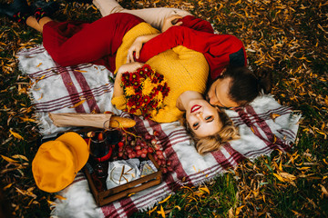 Amazing loving couple in the autumn park have a rest lying on a plaid, an autumn picnic with wine...