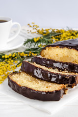 Squeezes of homemade homemade cake with chocolate icing in a section on a white background with a branch of mimosa nearby