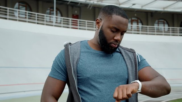 Man using smart watch on racetrack. Sportsman checking results after workout