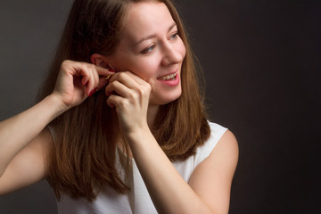 Brown-haired girl on a black background in white blouse. She laughs happily and Zips up her earring